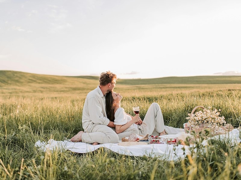A man and woman sitting on a blanket in a field