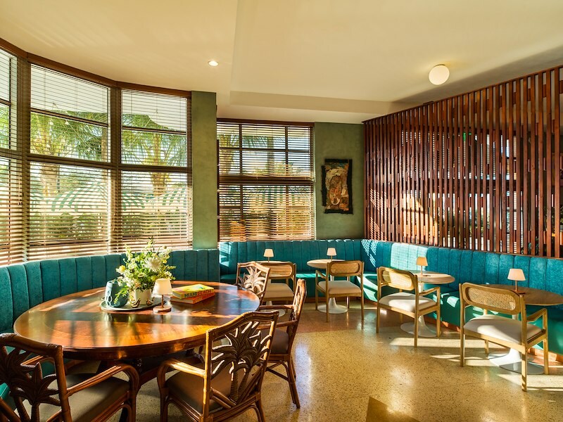 A dining area with teal bench seating, wooden tables and chairs, and large windows.