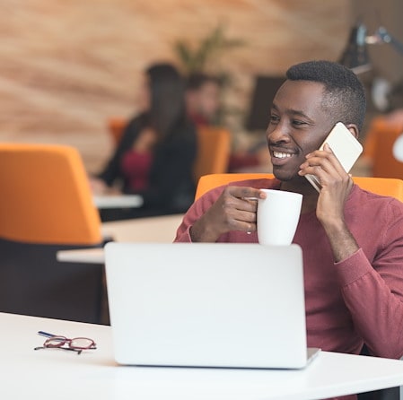 Man talking on the phone while holding a mug at his desk with a laptop