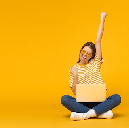 Air Academy Credit Union SEG eligibility image showing a woman celebrating while sitting with a laptop against a yellow background