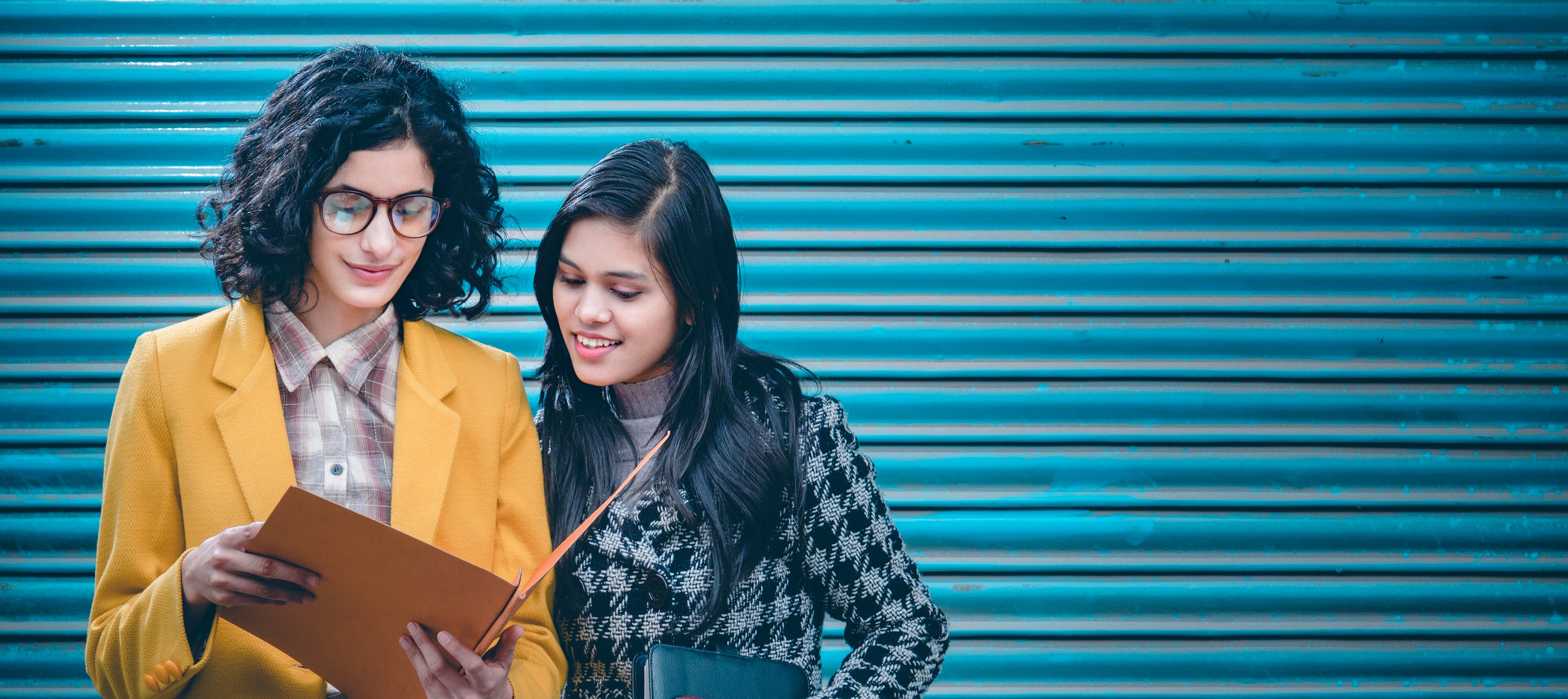 Two women standing together inspecting documents in a folder