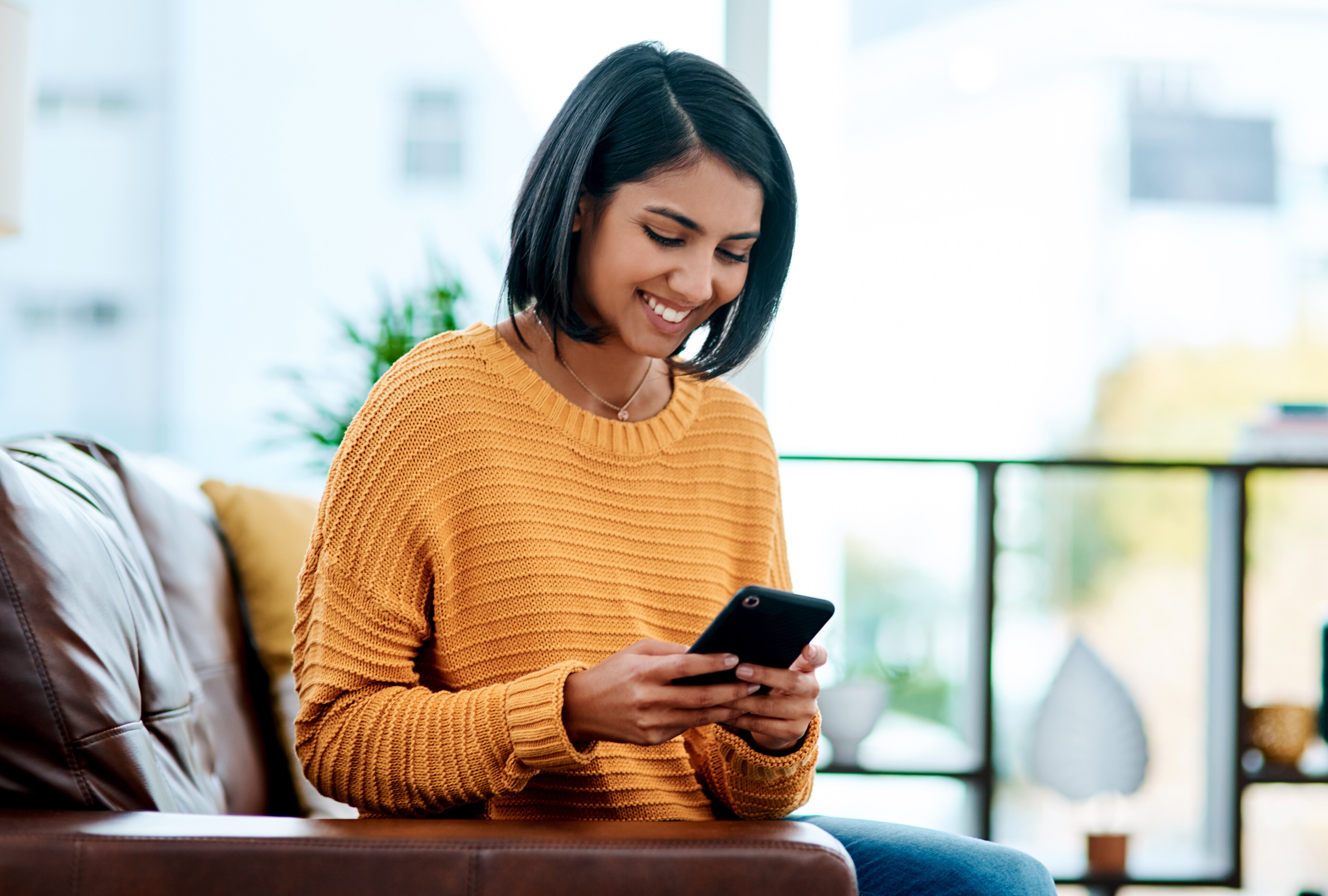 Woman sitting on leather couch holding smartphone