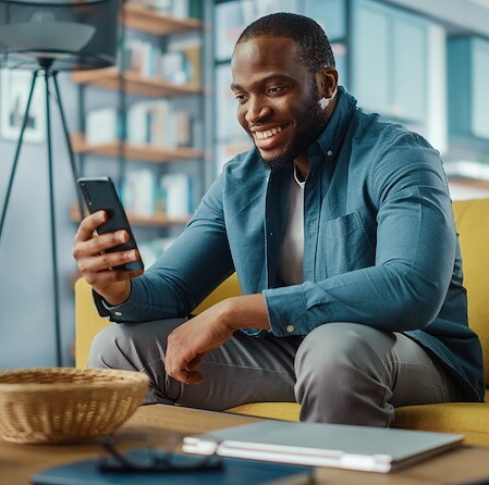Man Smiling While Using Smartphone On Living Room Sofa