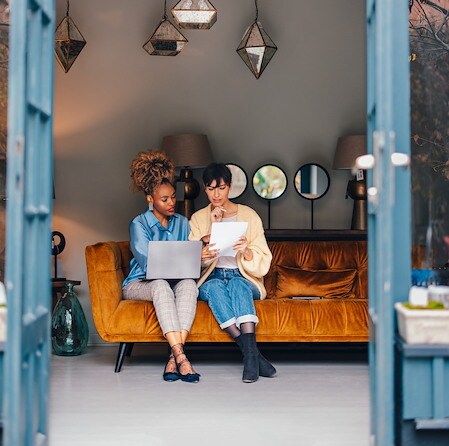 Two Business Partners Reviewing Documents And Laptop On Orange Sofa
