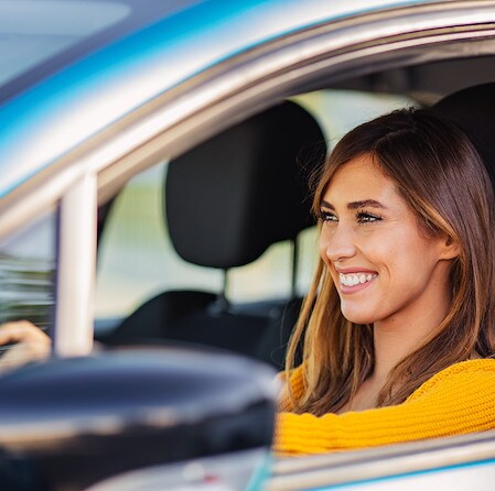 Woman smiling while driving a car, representing Air Academy Credit Union vehicle and loan protection services