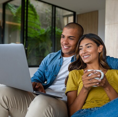 Smiling Couple Sitting Together Looking At Laptop At Home