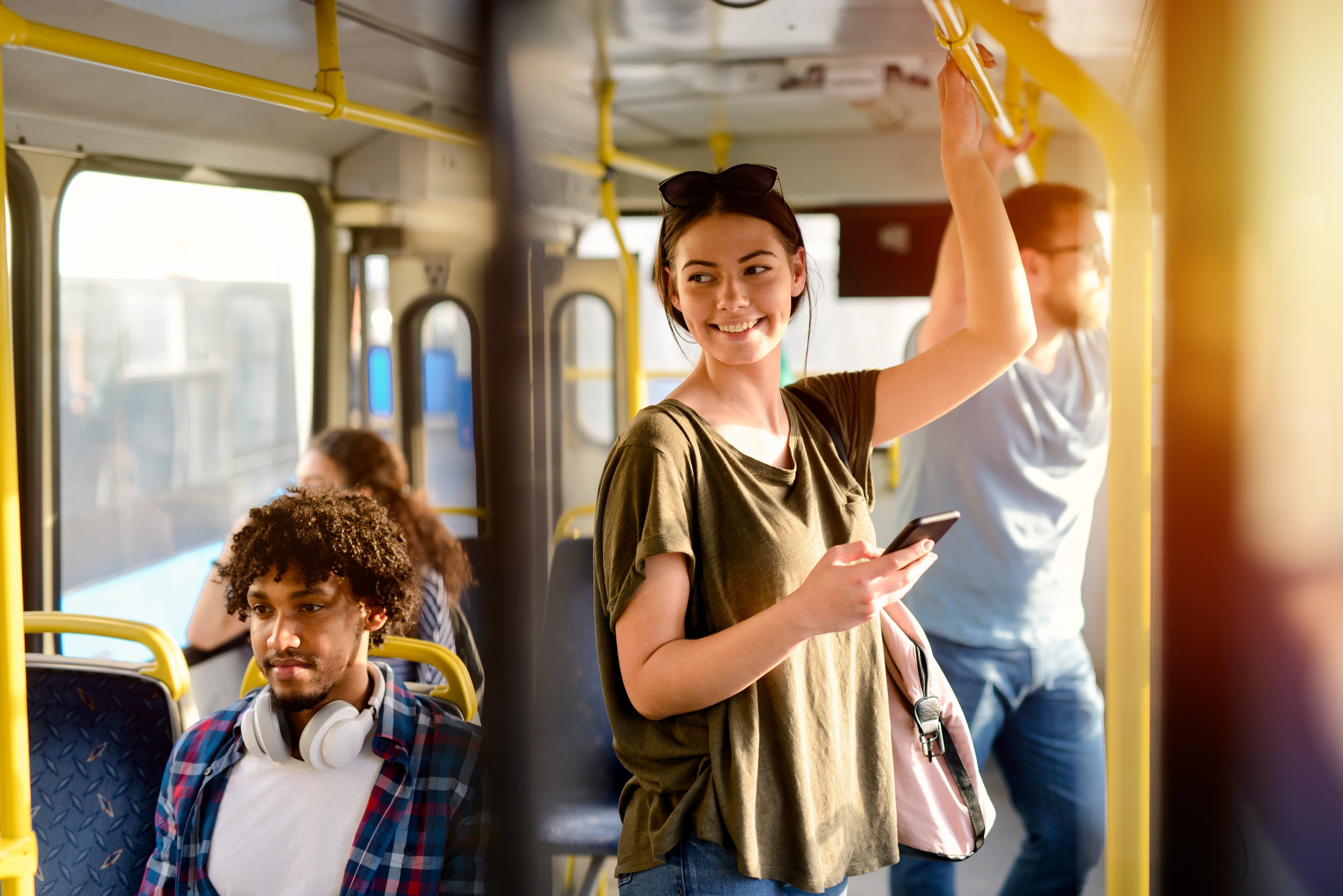 A smiling woman holding onto a handrail and looking at her smartphone while riding public transit