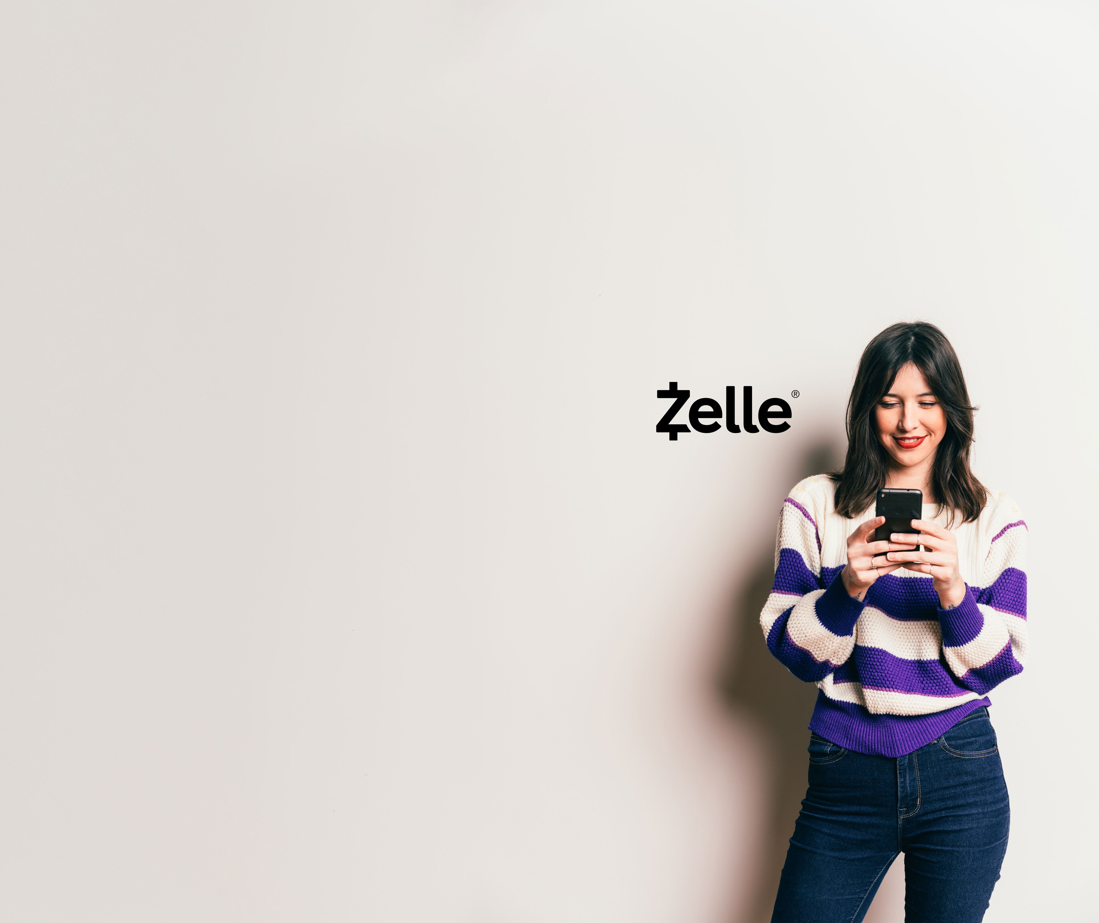 Smiling Woman Using Mobile Phone Next To Zelle Logo