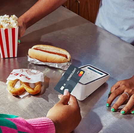 Person tapping a Greenlight debit card on a payment terminal next to food items