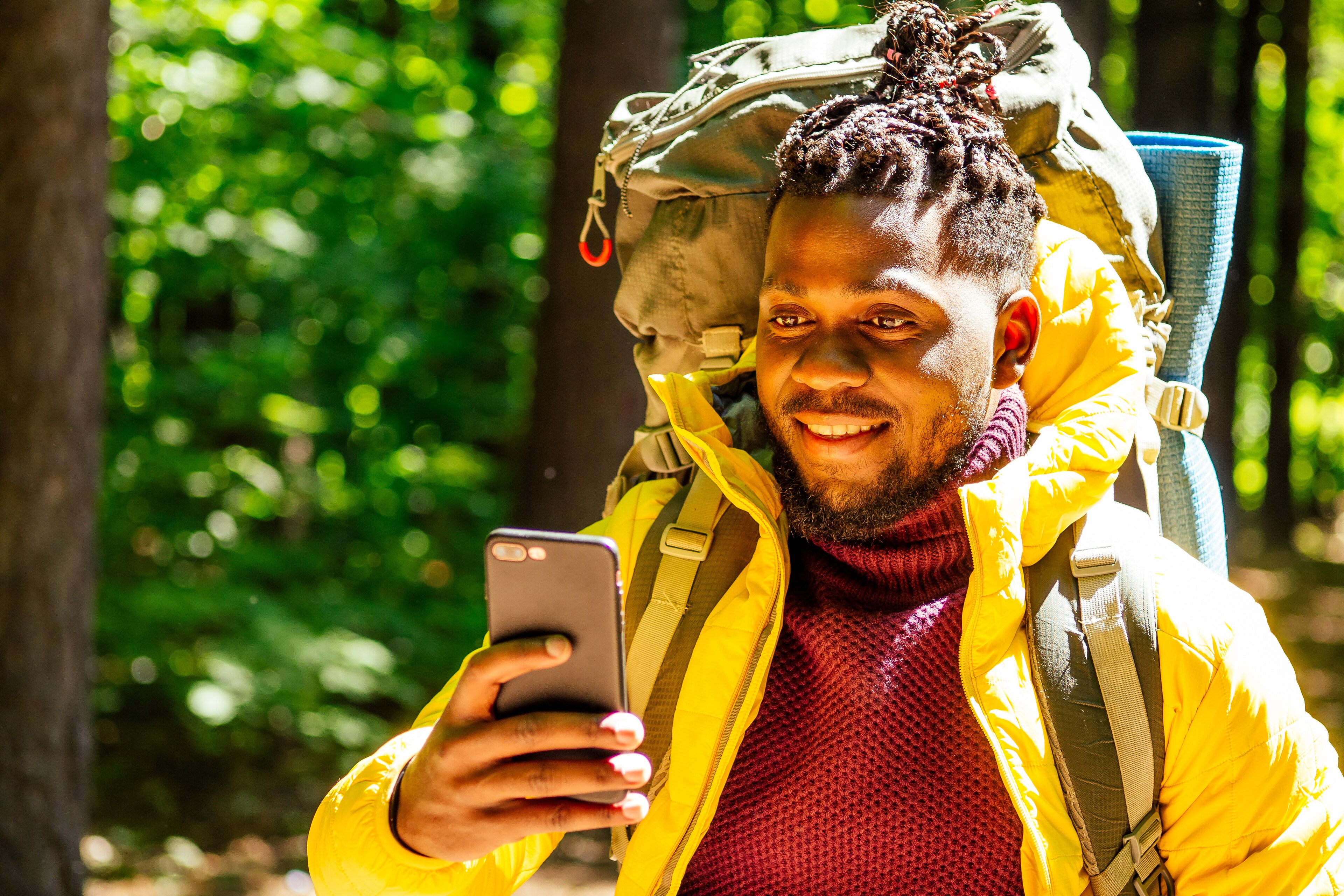 Smiling hiker with a backpack and yellow jacket looking at his smartphone in the woods
