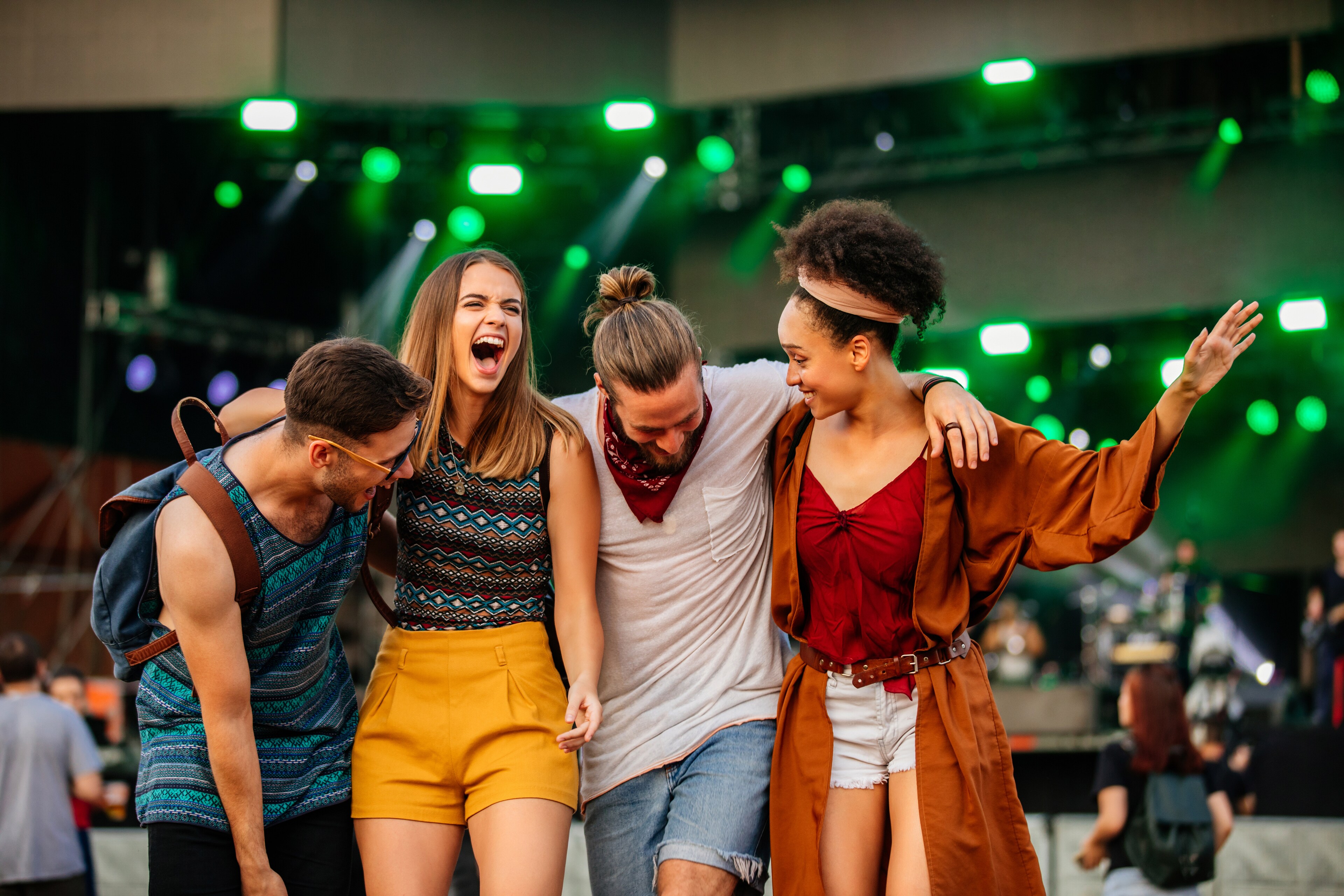 Group of four cheerful young adult friends laughing and walking together at an outdoor evening festival