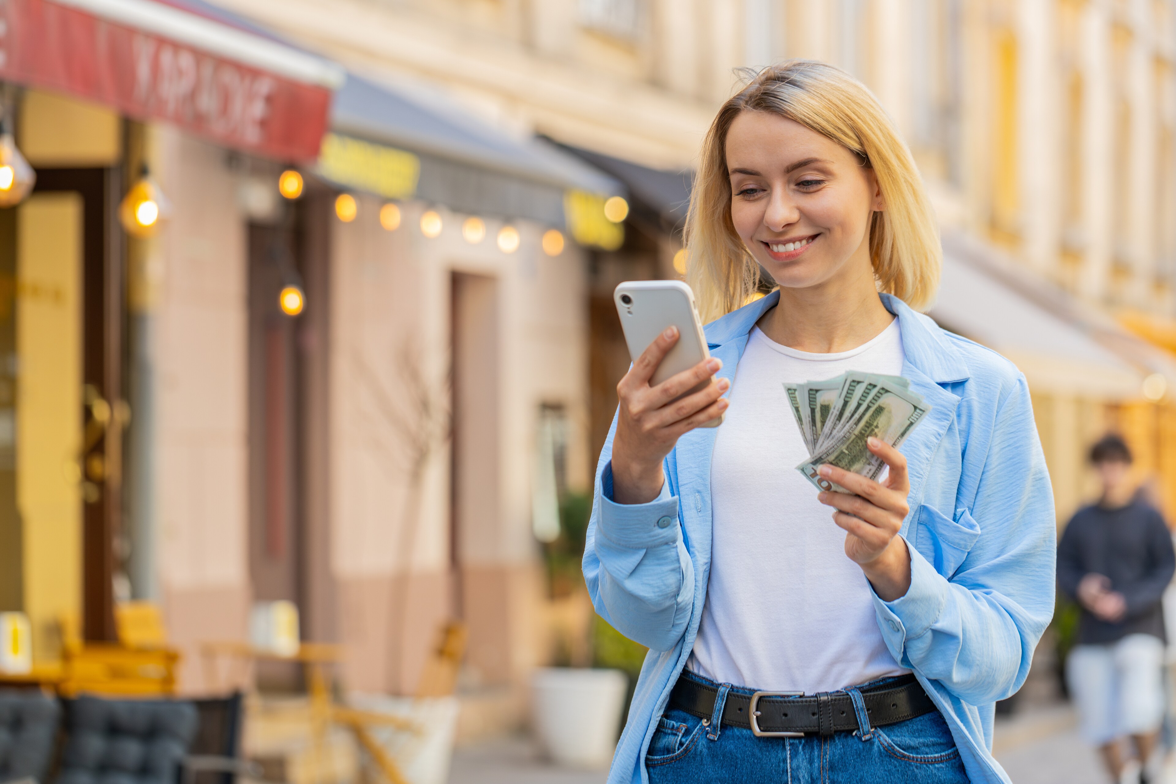 Woman holding cash while looking at smartphone on city street