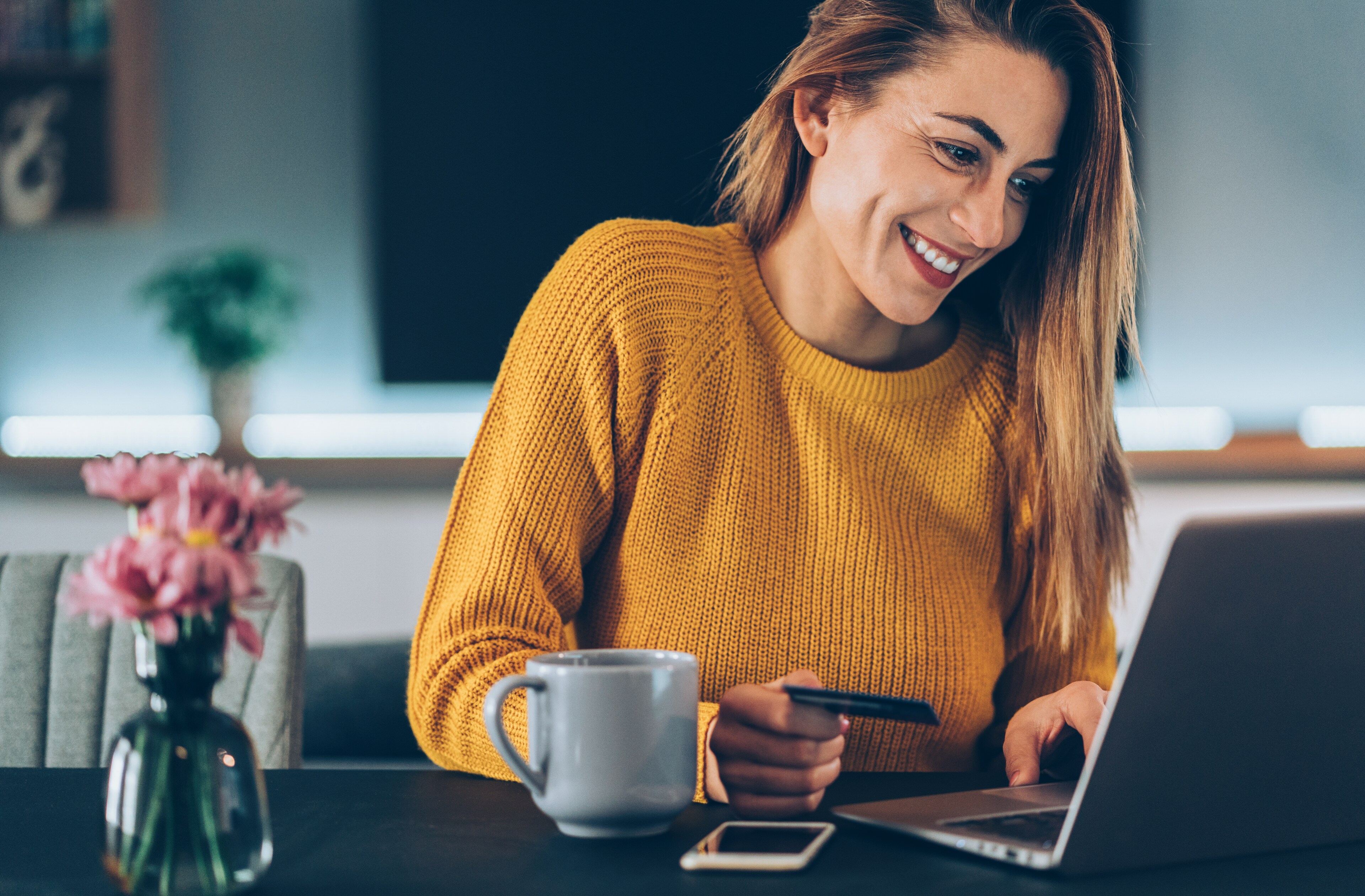 Woman holding payment card while typing on laptop near a coffee mug