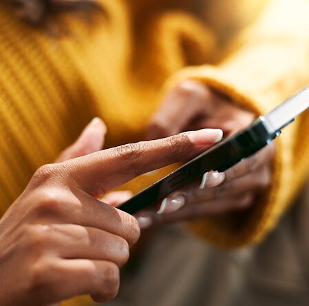 Close-up of a person in a mustard sweater using a smartphone, finger poised over the screen, conveying focused everyday digital connection.