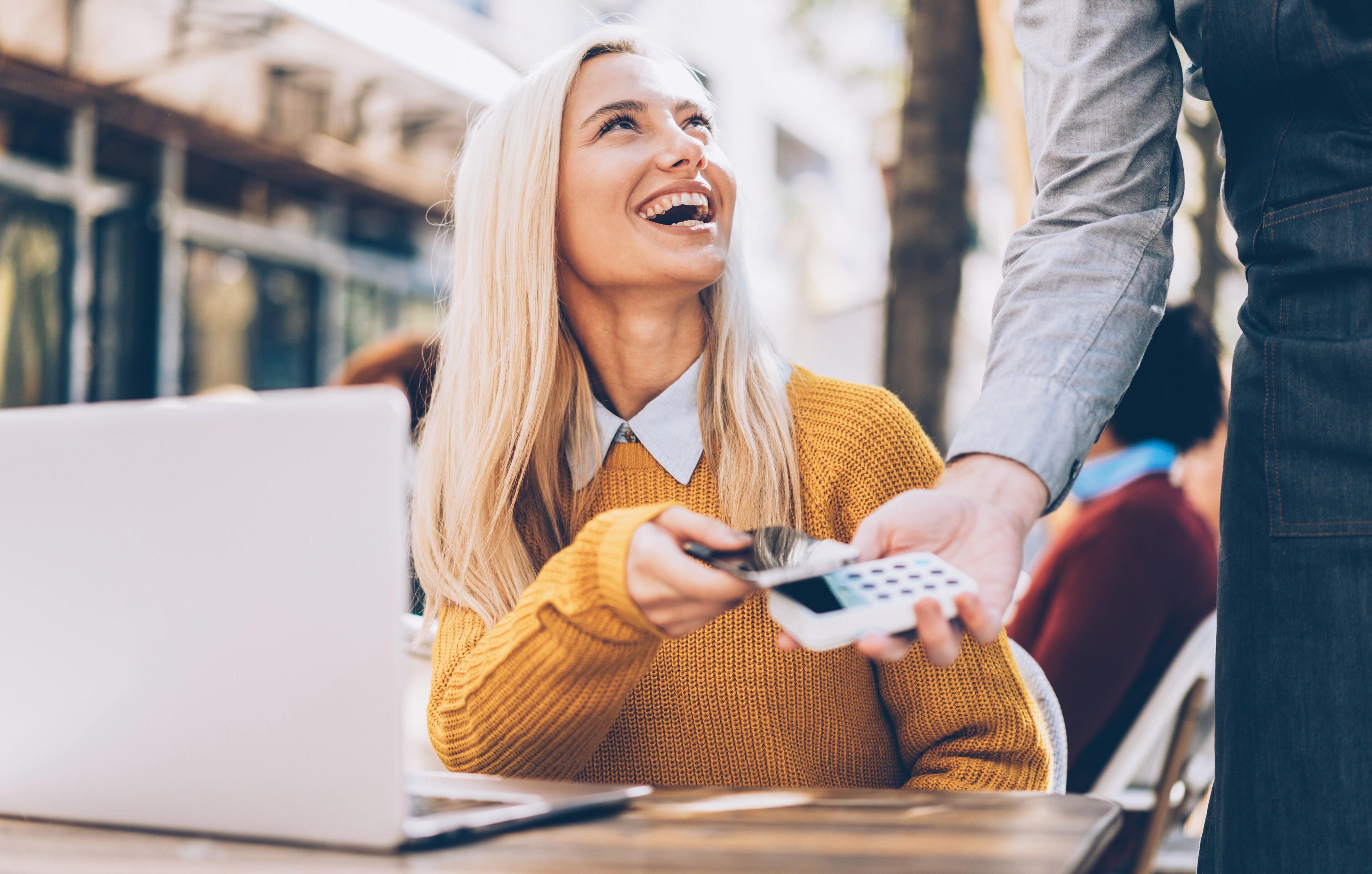 Happy woman paying contactless with smartphone at an outdoor cafe
