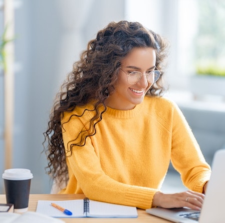 Smiling Woman With Curly Hair Typing On Laptop At Desk