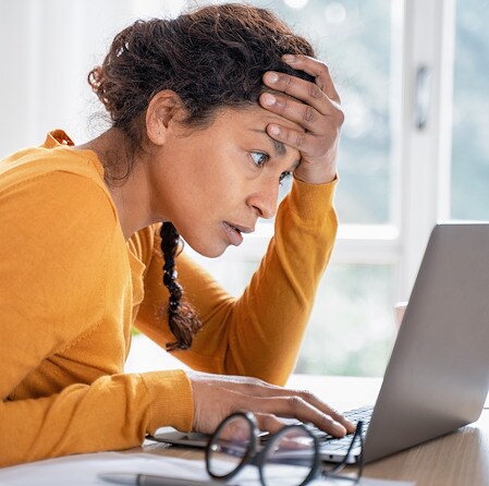Stressed Woman Holding Forehead Looking At Laptop Screen At Desk