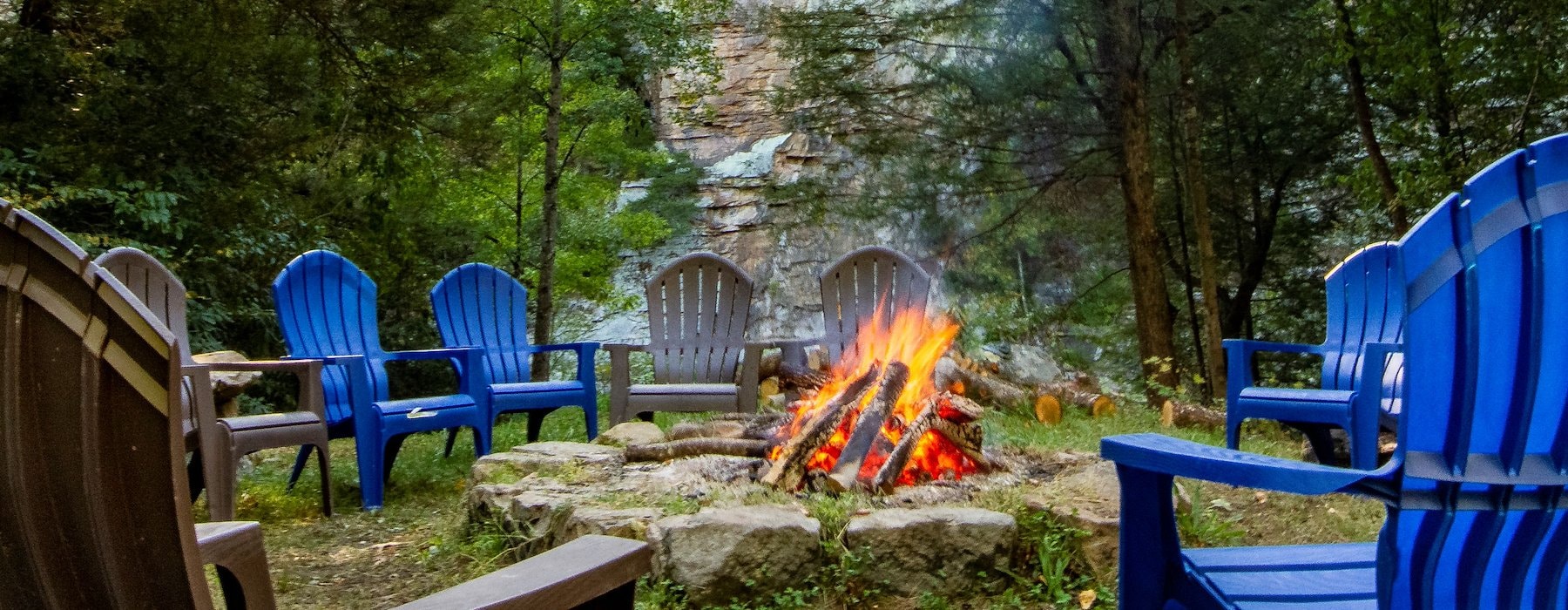 A cozy outdoor campfire surrounded by blue and brown Adirondack chairs Adventures on the Gorge - Lansing West Virginia USA