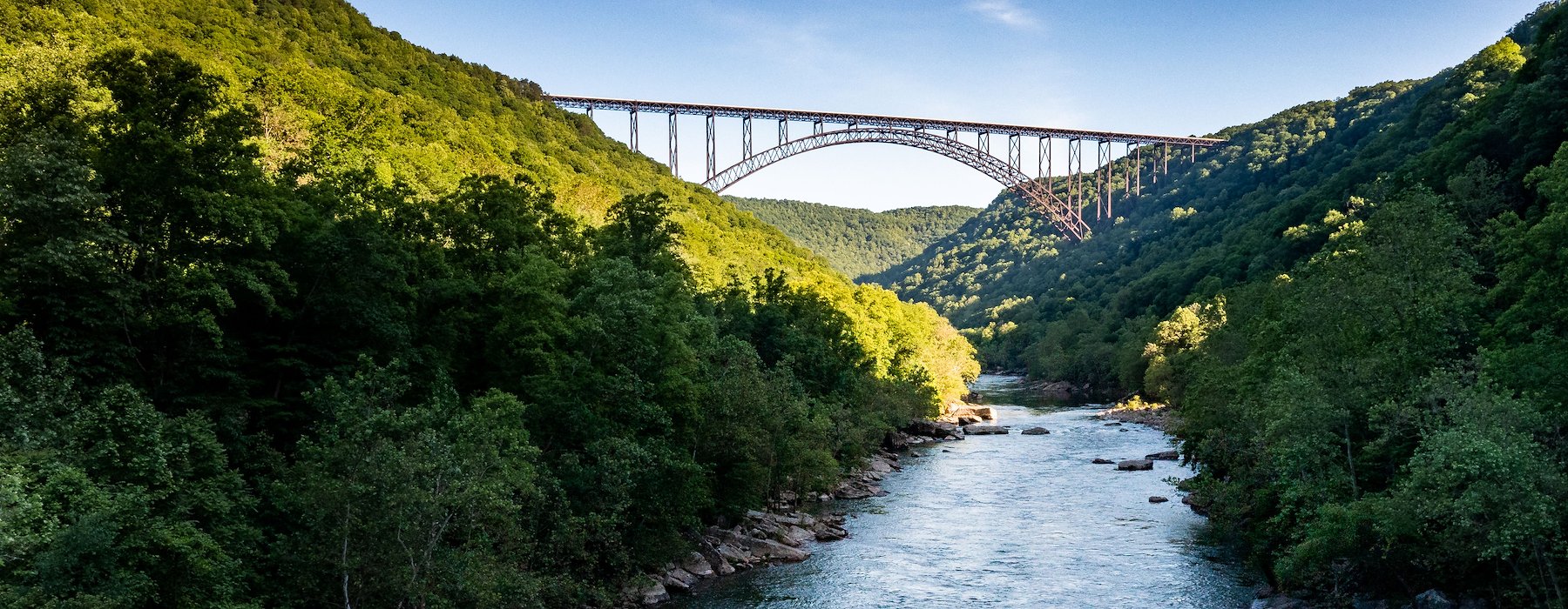 A serene river flows between lush green mountains under a clear blue sky Adventures on the Gorge - Lansing West Virginia USA
