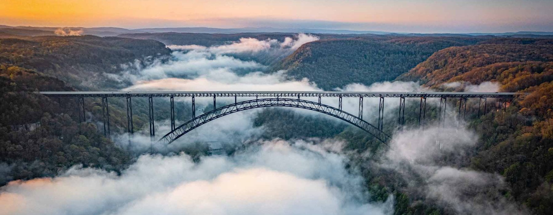 A steel arch bridge spans a fog filled gorge with dense Adventures on the Gorge - Lansing West Virginia USA