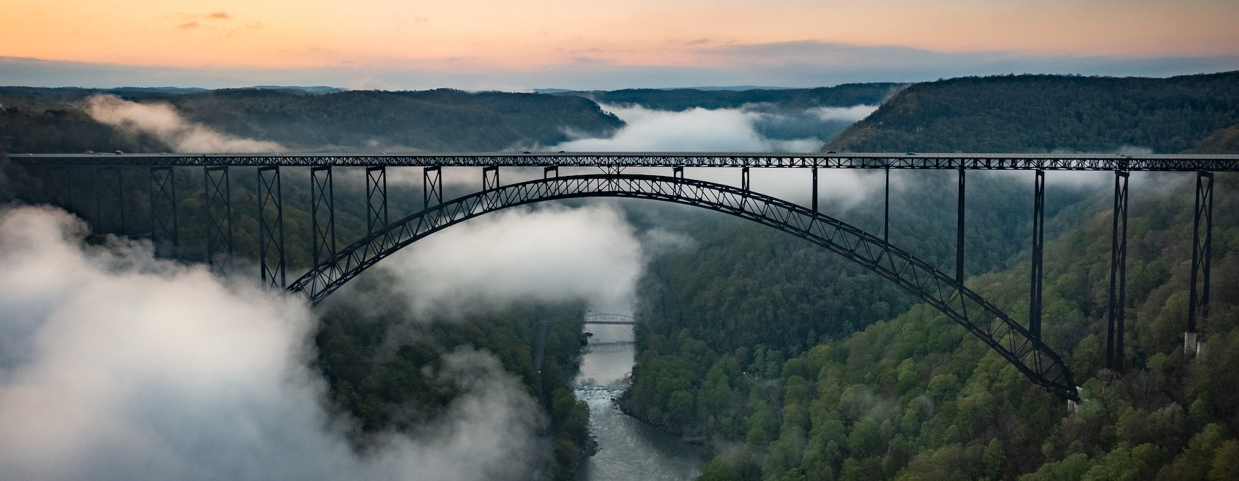 A steel arch bridge stretches over a misty valley Adventures on the Gorge - Lansing West Virginia USA