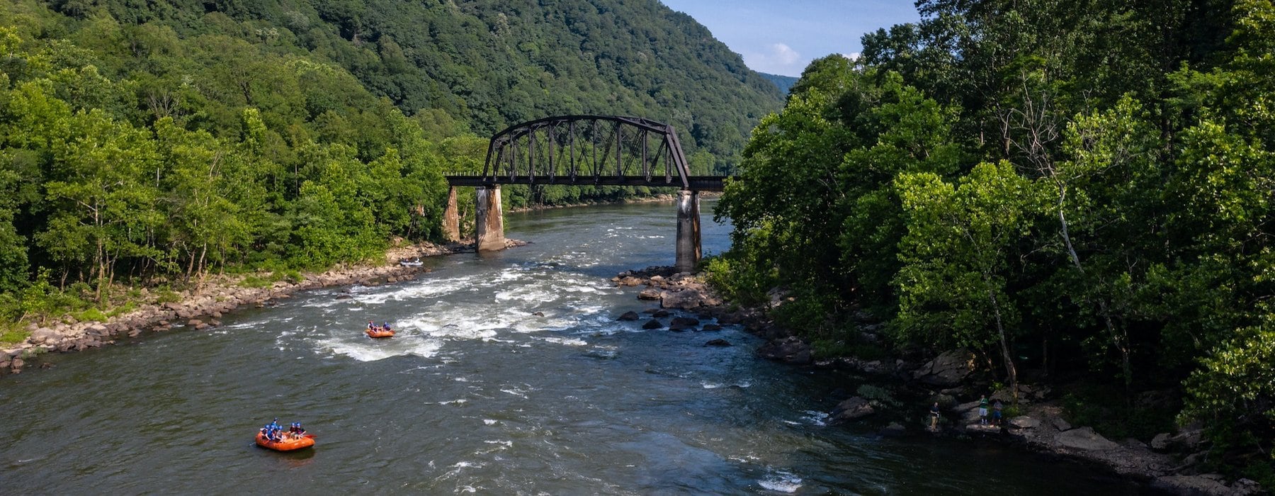 River with rapids and several orange rafts under a metal bridge Adventures on the Gorge - Lansing West Virginia USA
