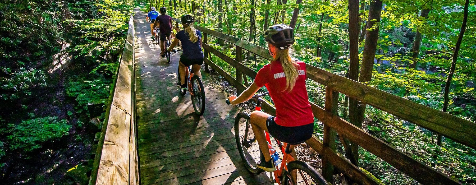 Three cyclists ride bicycles across a wooden bridge surrounded Adventures on the Gorge - Lansing West Virginia USA