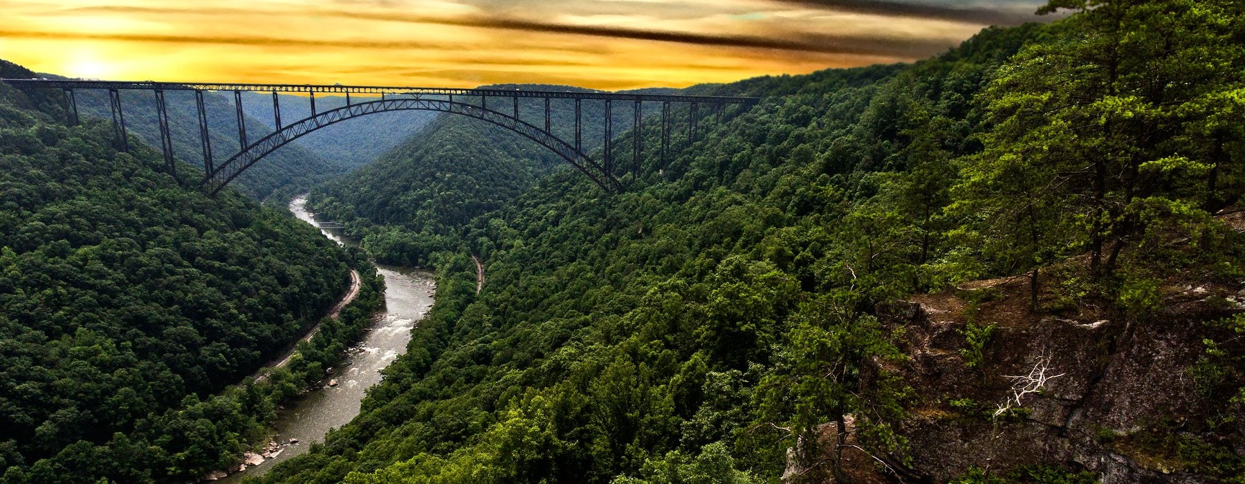 A majestic arched bridge spans a lush green valley with a winding river Adventures on the Gorge - Lansing West Virginia USA