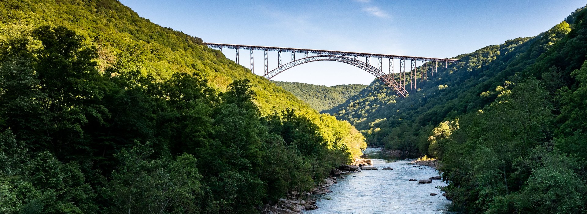 Boat sails along a river framed by lush green hills beneath a towering arched bridge Adventures on the Gorge - Lansing West Virginia USA