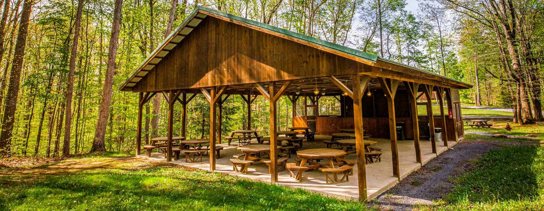 Wooden pavilion in a sunlit forest with picnic tables inside and dappled Adventures on the Gorge - Lansing West Virginia USA
