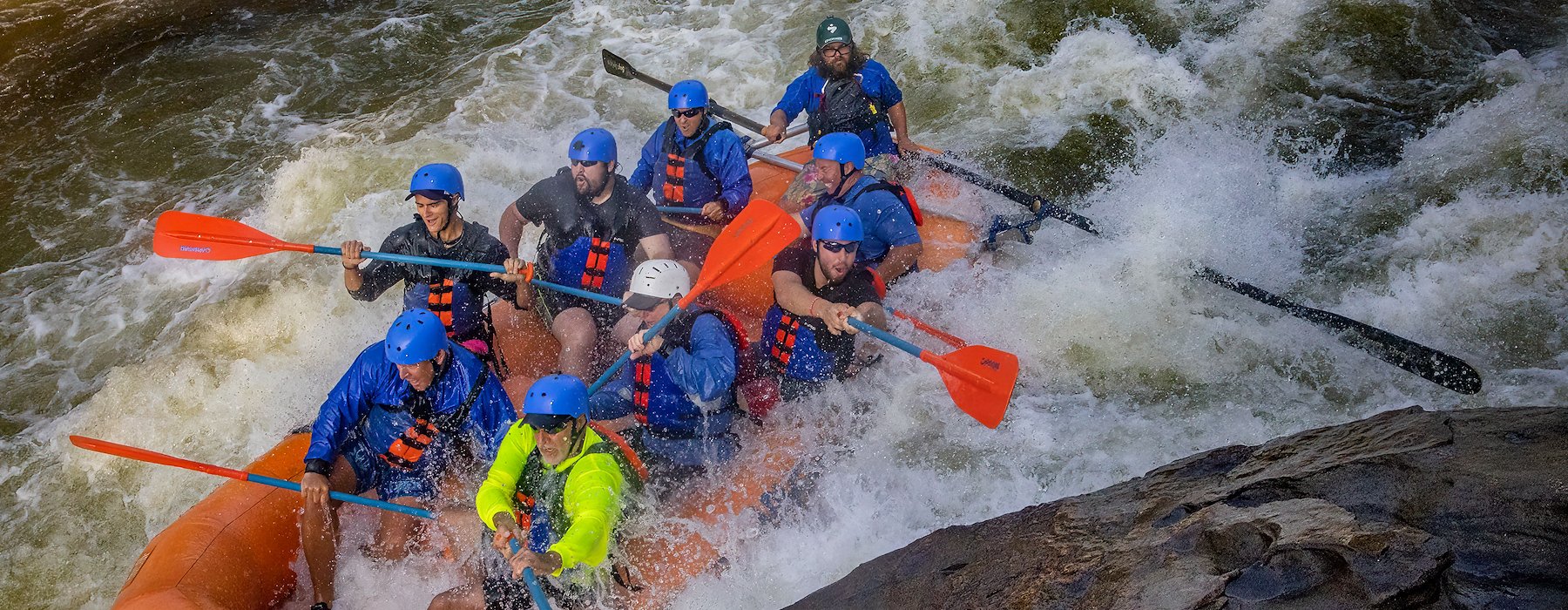 Several individuals in an orange raft navigating a rapid river Adventures on the Gorge - Lansing West Virginia USA