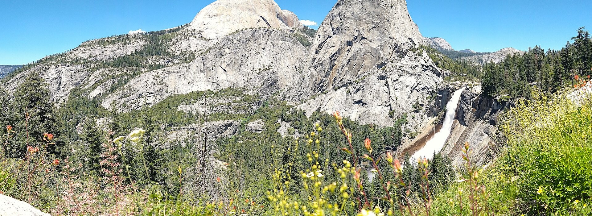 Hikers with backpacks walk along a rocky trail through a green meadow Yosemite National Park Lodging and Activities - California - United States