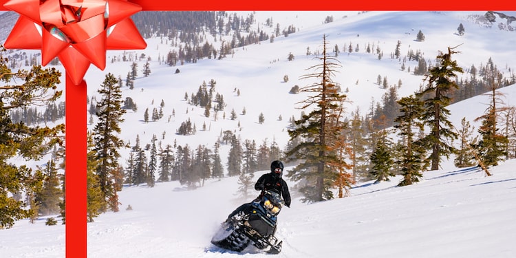 A person on a snowmobile going down a snowy hill with a red ribbon