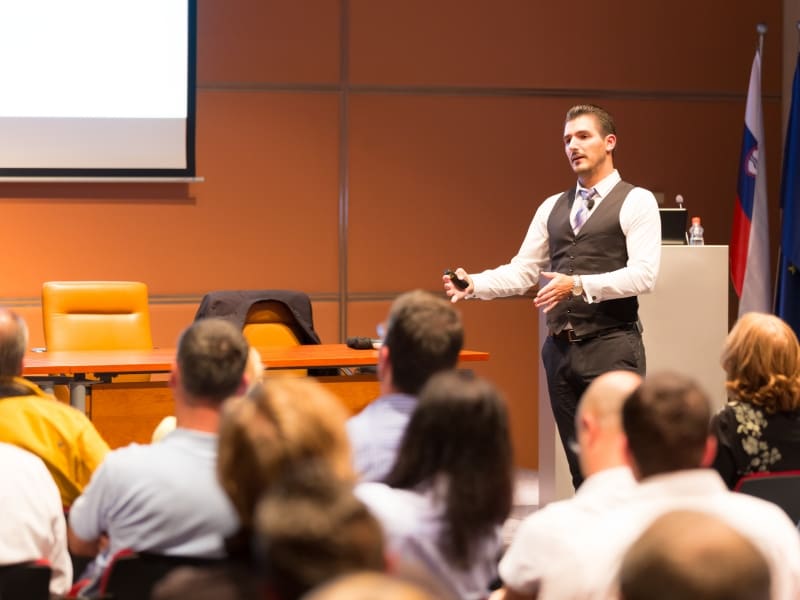 A man in a suit giving a presentation to an audience in a meeting room.