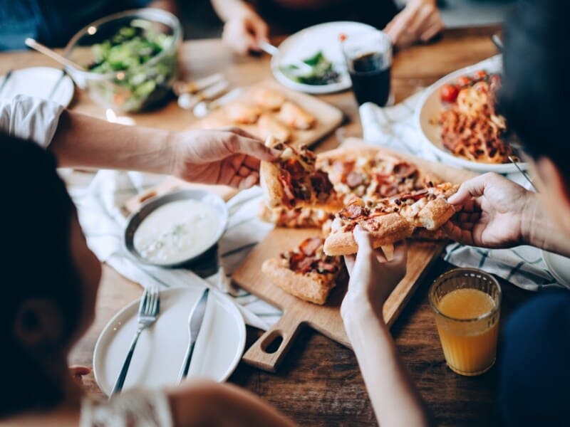 A group of people sharing a meal with pizza and other dishes on a wooden table.