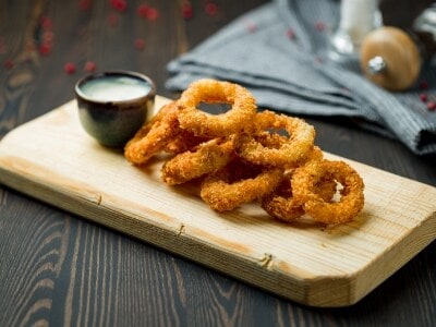 A wooden board with fried onion rings and a small bowl of dipping sauce