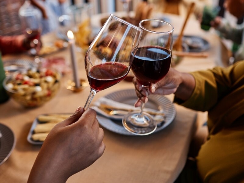 Two people are clinking wine glasses at a table with food.