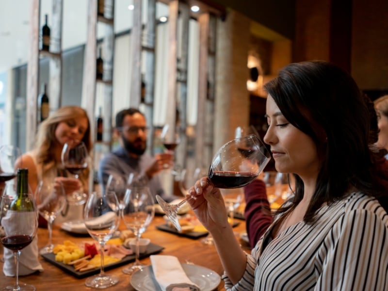 A group of people sitting at a table, tasting wine and eating food.