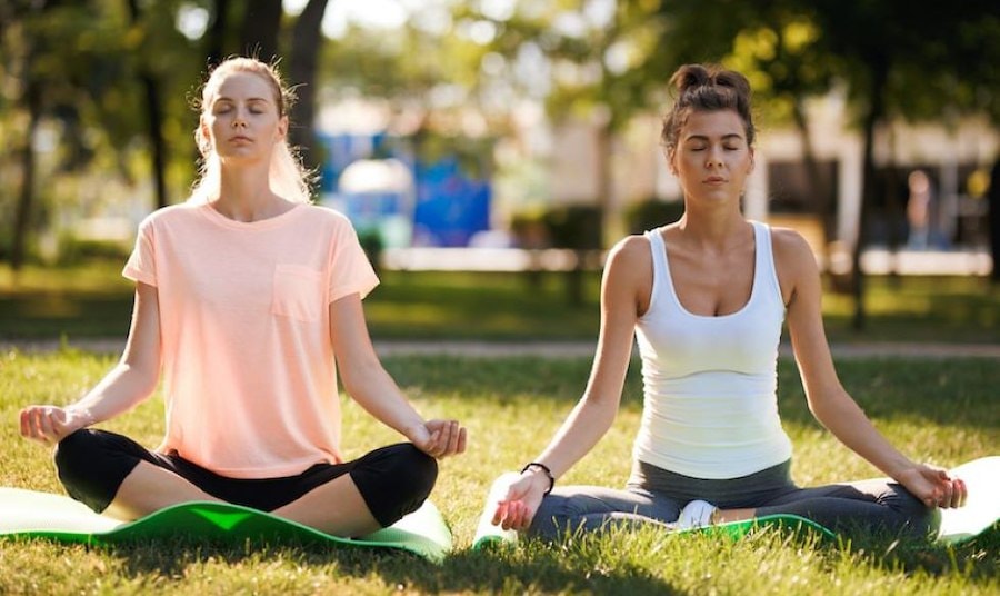 Two women sitting on mats in the grass