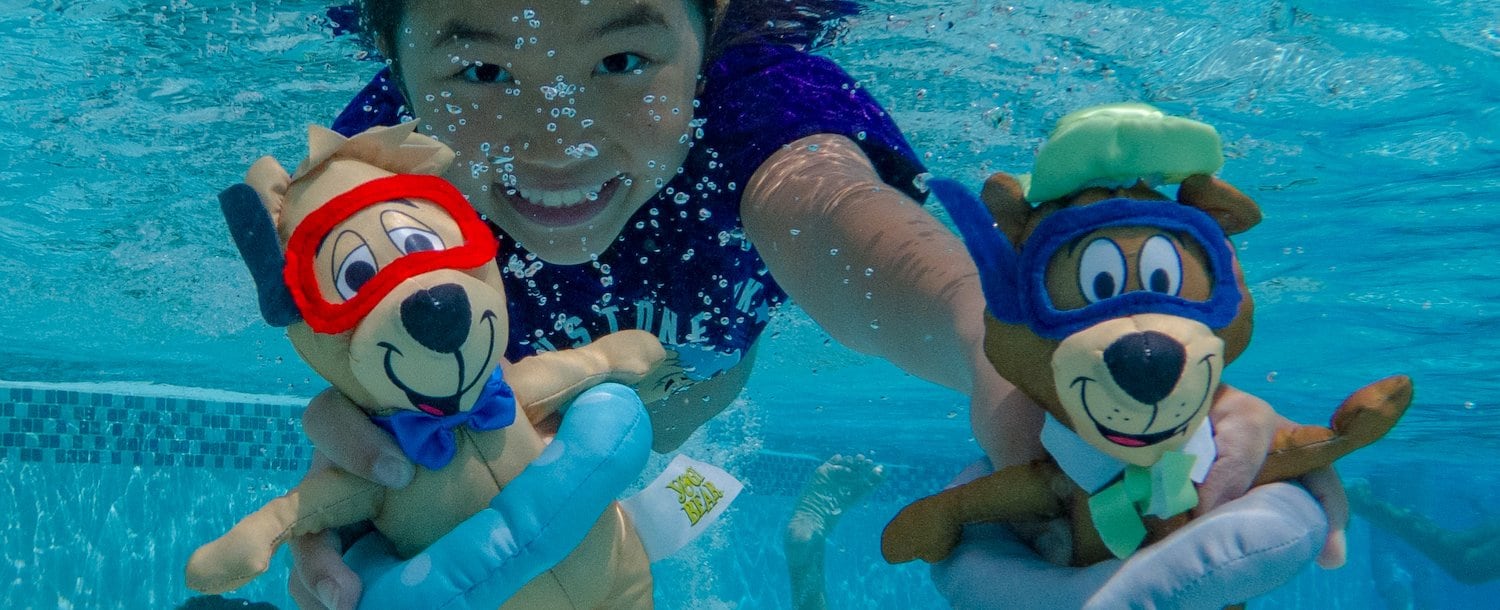 A group of people swimming in a pool with stuffed animals at Jellystone Park™ Williamsburg