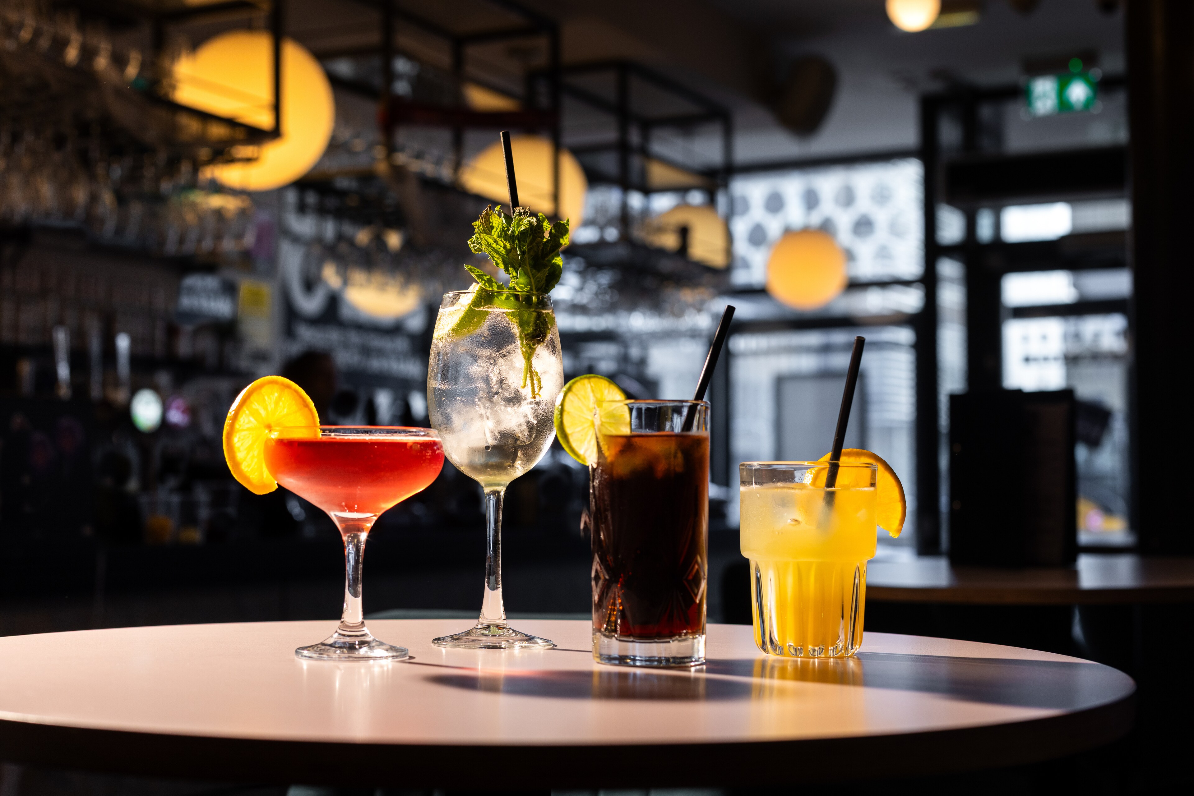 Colorful cocktails garnished with citrus and mint displayed on a table in a bar.