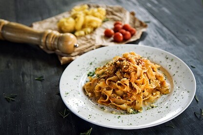 A plate of pasta topped with sauce and grated cheese is served on a rustic table with fresh ingredients nearby.