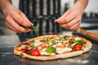 A chef adds fresh greens to a pizza topped with melted cheese, vegetables, and herbs.