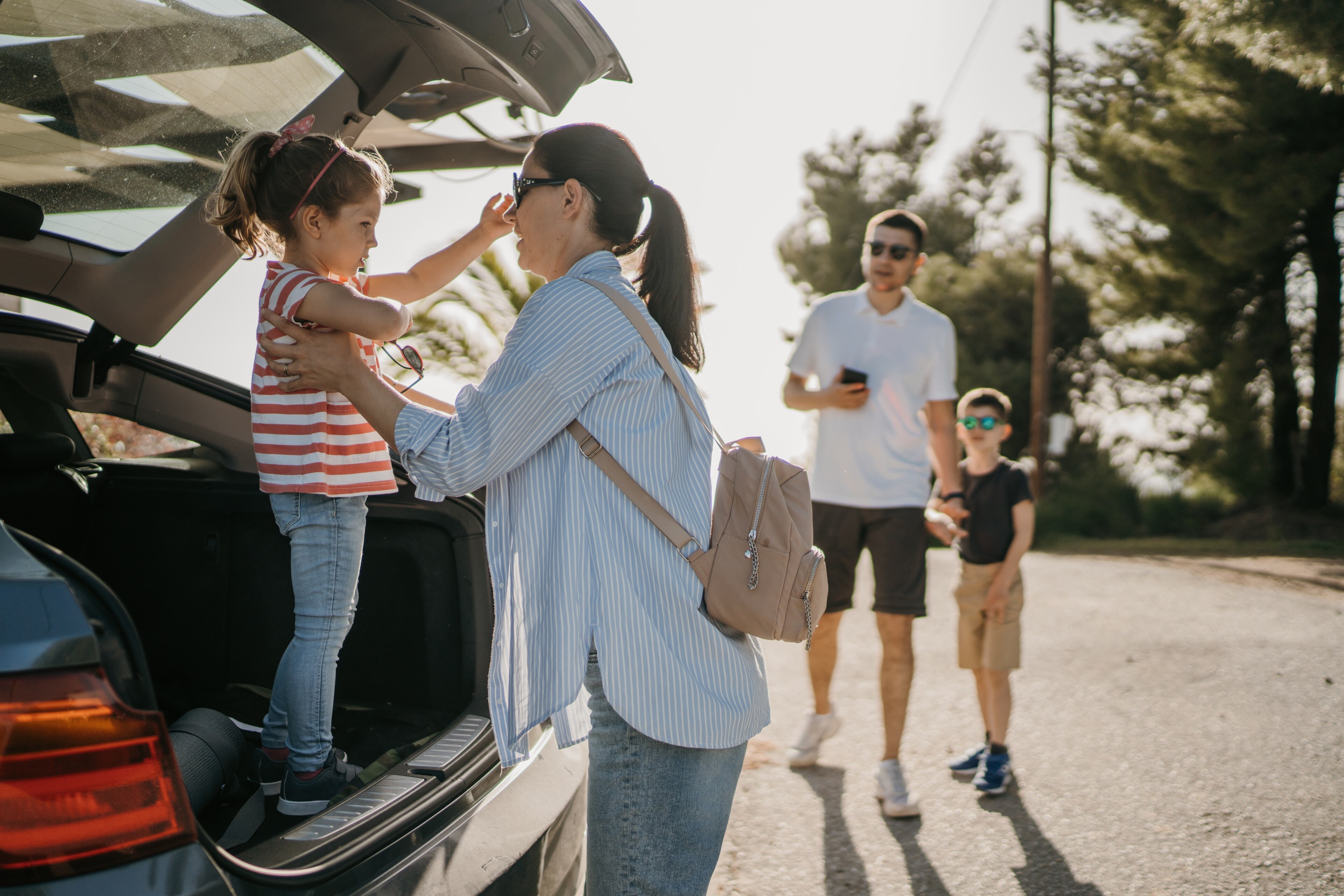 Family preparing for a road trip beside an open vehicle trunk outdoors