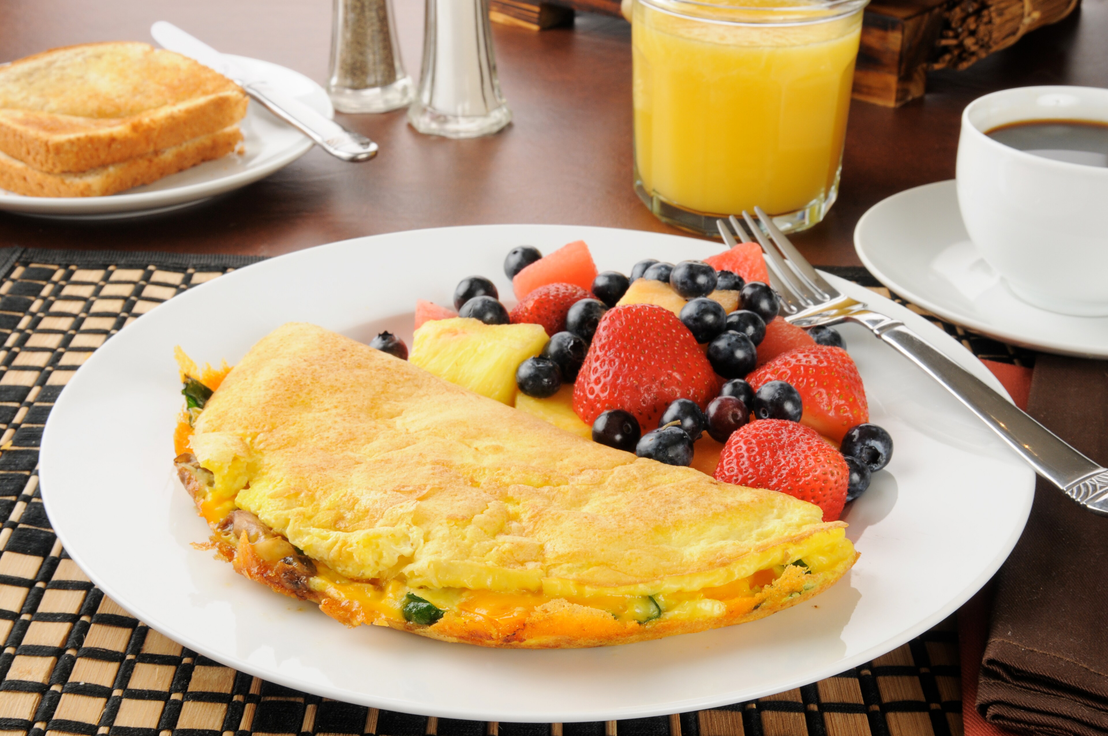 Breakfast plate with an omelet, fresh fruits, juice, coffee, and toast on a dining table