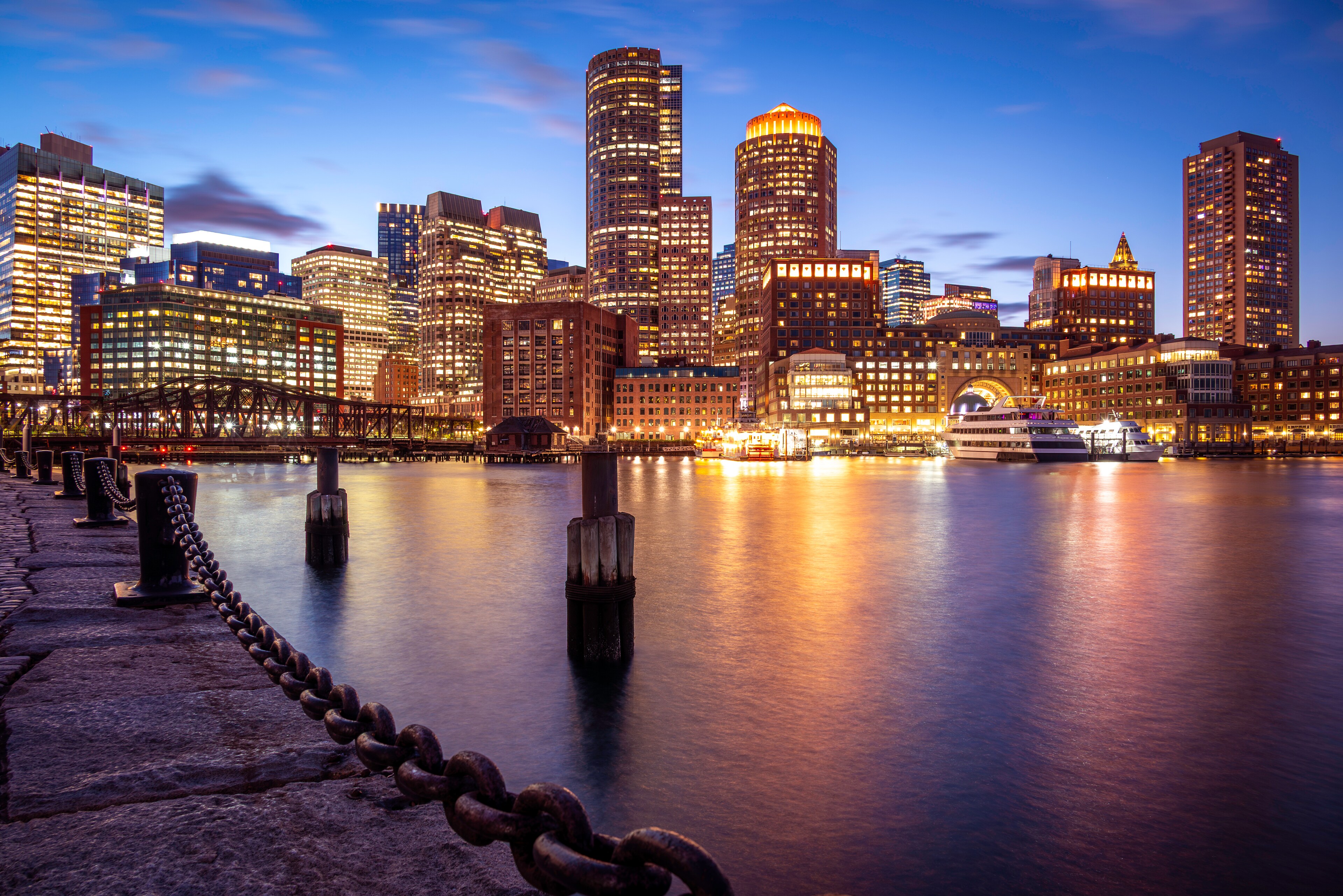 Boston Harbor waterfront skyline illuminated at dusk with city lights reflecting on the water in Boston, MA.