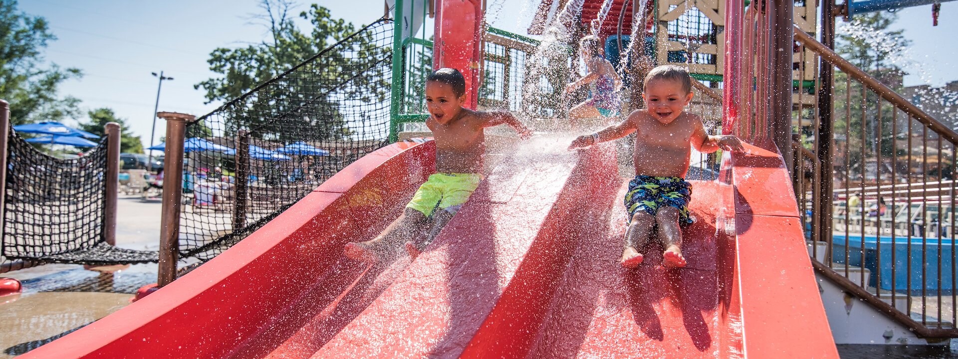 Two young children joyfully slide down a water slide at a sunny outdoor water park, Chula Vista Resort, Wisconsin 