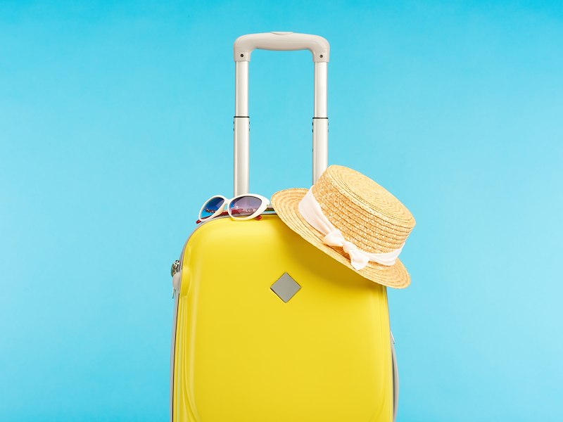 A yellow suitcase with a straw hat and sunglasses