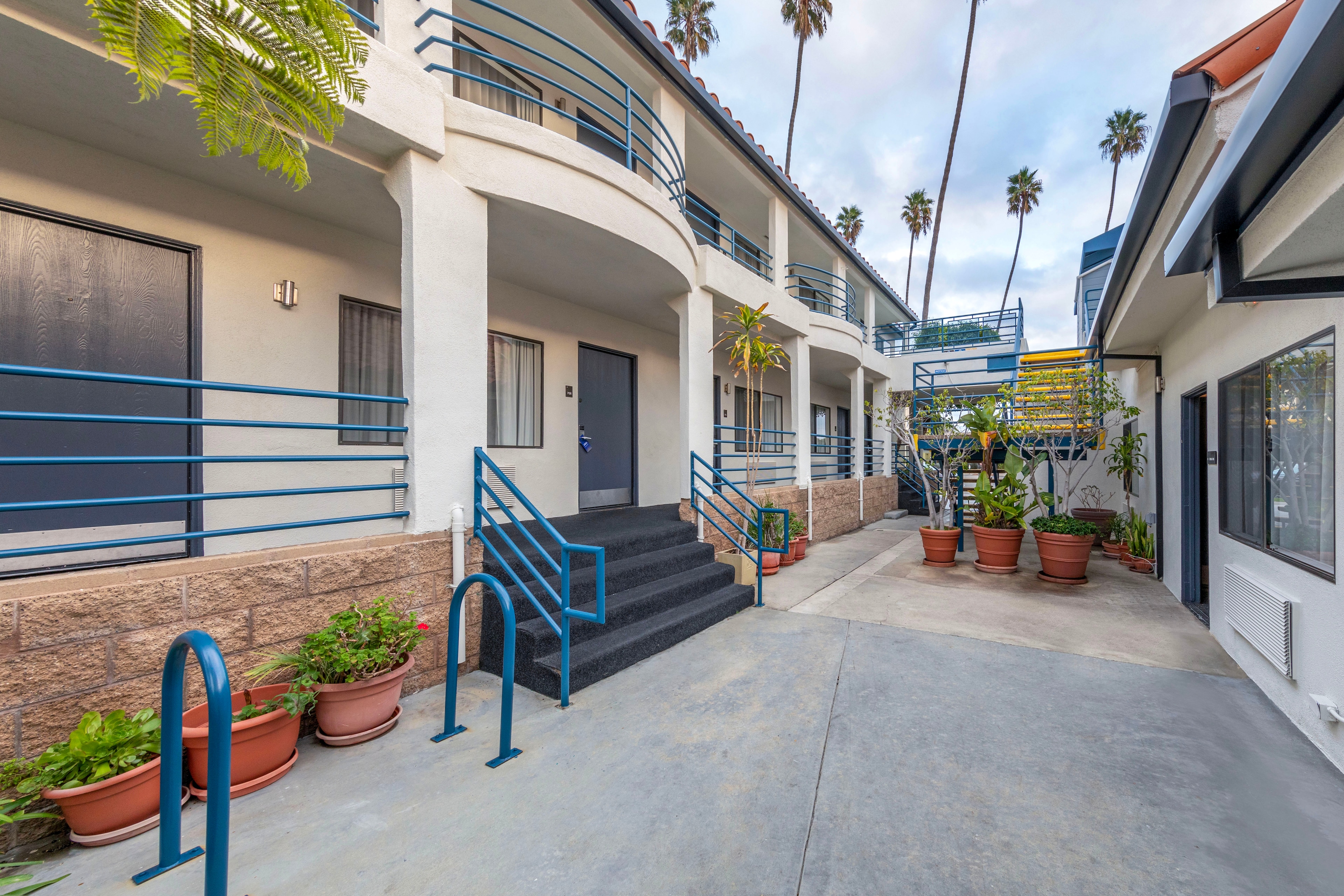 Outdoor corridor of a motel with two stories, blue railings, and stairs leading to dark doors