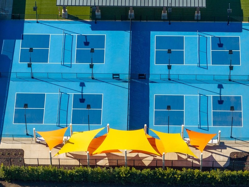 A tennis court with blue and yellow shade sails